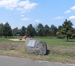 Blick zum Gedenkstein, umgeben von Grünanlage mit Spielplatz