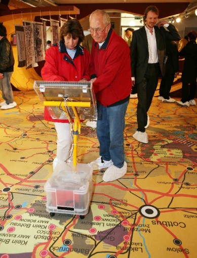 Foto: Ausstellungsbesucher nutzen den Infosauger auf dem Kartenteppich. Foto: Ausstellungsbesucher nutzen den Infosauger auf dem Kartenteppich.