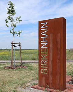 Blick auf die Cortenstahl- Stele mit der Inschrift Birkenhain. Blick auf die Cortenstahl- Stele mit der Inschrift Birkenhain.