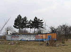 Gestrandetes Schiff in der Landschaft bepflanzt mit 4 Nadelbäumen und einer Rumpfbeschriftung: Die Wüste ist in uns.