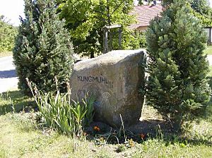 Gedenkstein mit der Inschrift "Klingmühl1487"umgeben von Blumen und Sträuchern 