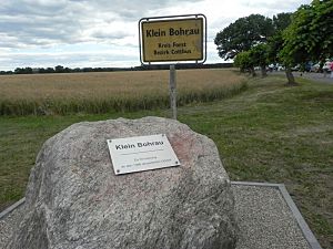 Blick auf das ehemalige Ortseingangsschild von Klein Bohrau und auf den Gedenkstein mit der Tafelinschrift: Klein Bohrau, zur Erinnerung an den 1986 devastierten Ortsteil.