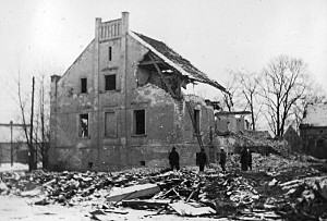 Einige Personen stehen vor dem teilweise zerstörten Gutshaus. Schnee bedeckt die Trümmer.