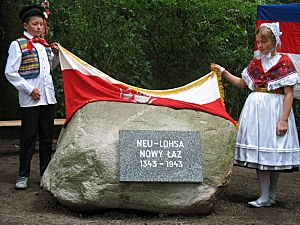 Blick auf den Gedenkstein, zwei Kinder in Hoyerswerdaer Festtagstracht enthüllen den Gedenkstein für Neu- Lohsa.