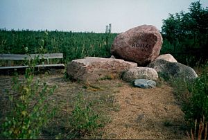 Gedenkstein mit der Inschrift  1350-Roitz-1976 umgeben von jungen Kiefern 