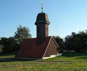 Auf einer Wiese umgeben von Bäumen steht die Kirchturmhaube.