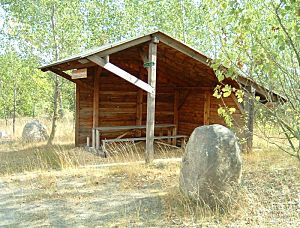 Schutzhütte mit Sitzplätzen umgeben von Laubbäumen und Findlingen